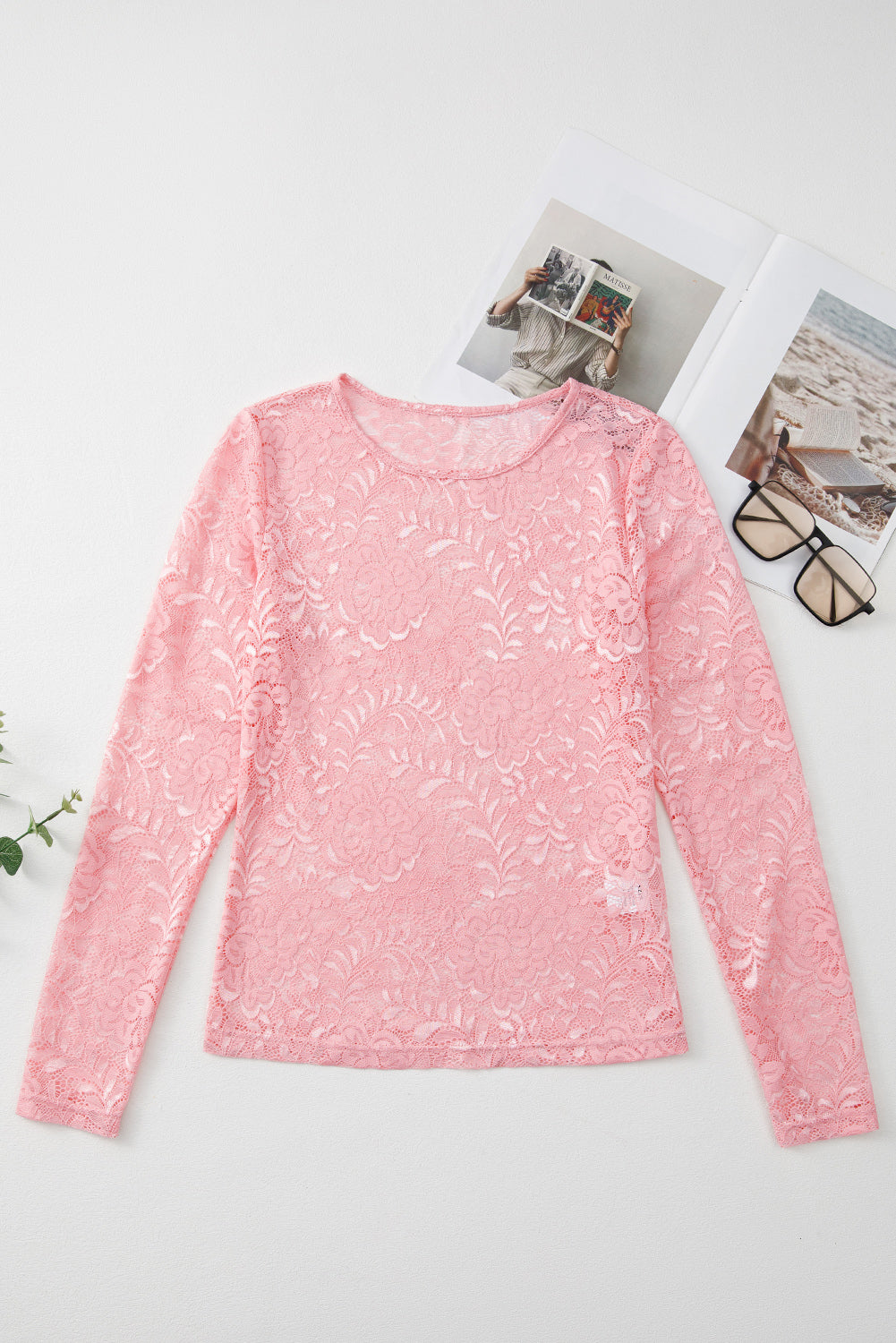 Pink lace long-sleeve top on a white surface with a magazine and glasses.