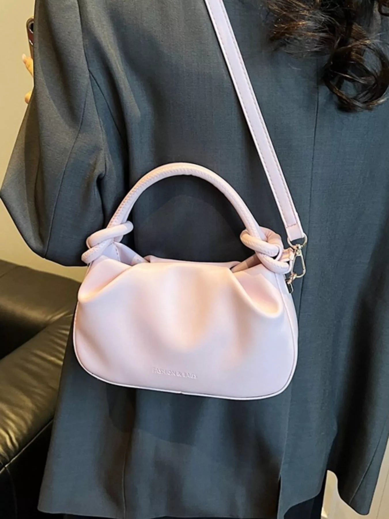 Light pink handbag with a strap over a person wearing a dark gray outfit.
