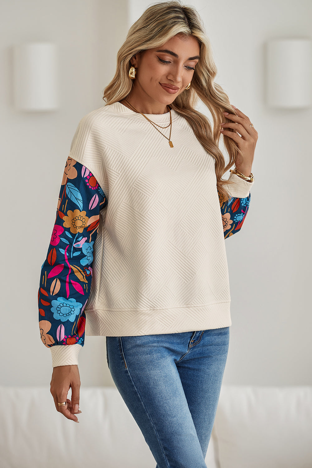 Woman wearing a cream sweater with colorful floral sleeves against a white background