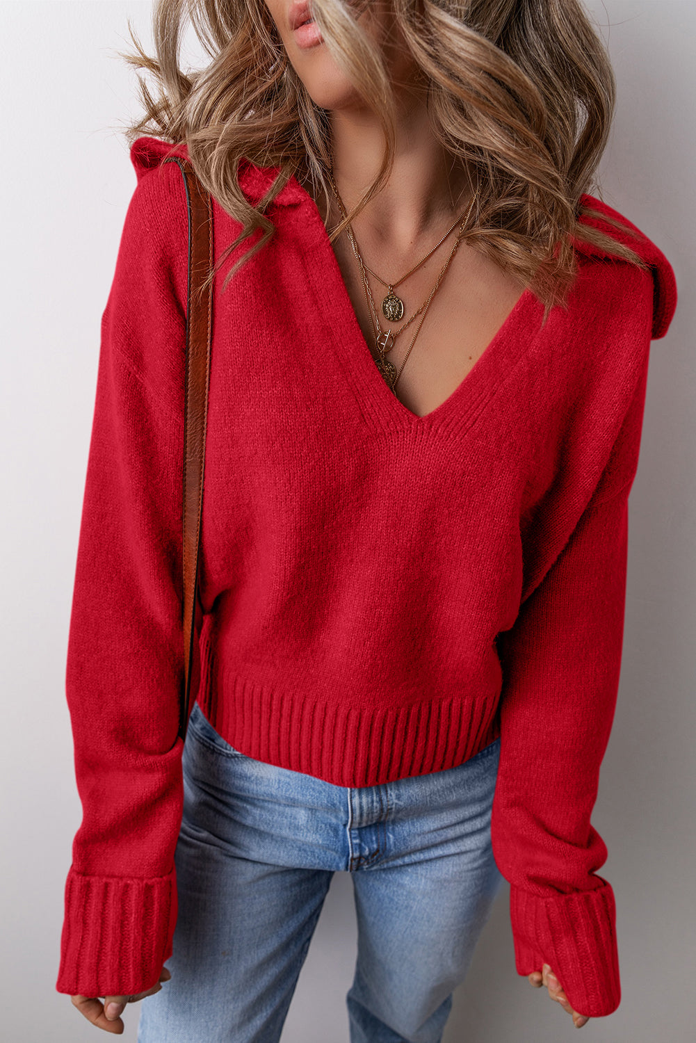 A woman wearing a racing red Ribbed V-Neck Sweater, paired with light blue jeans and layered gold necklaces.