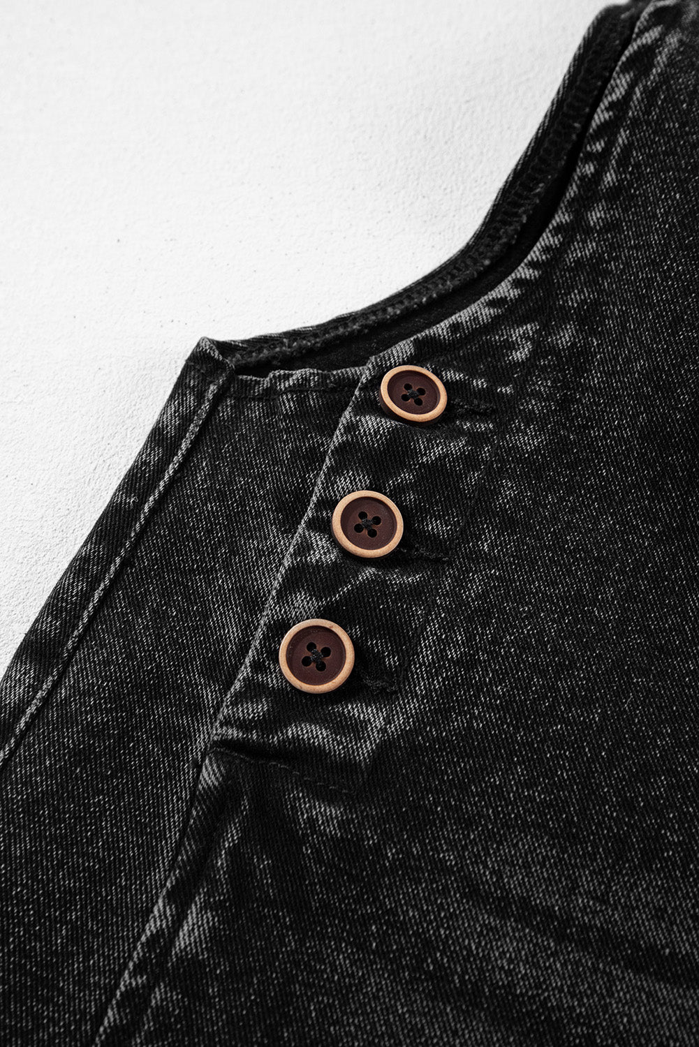 Close-up of a black denim shirt with brown buttons on a white background