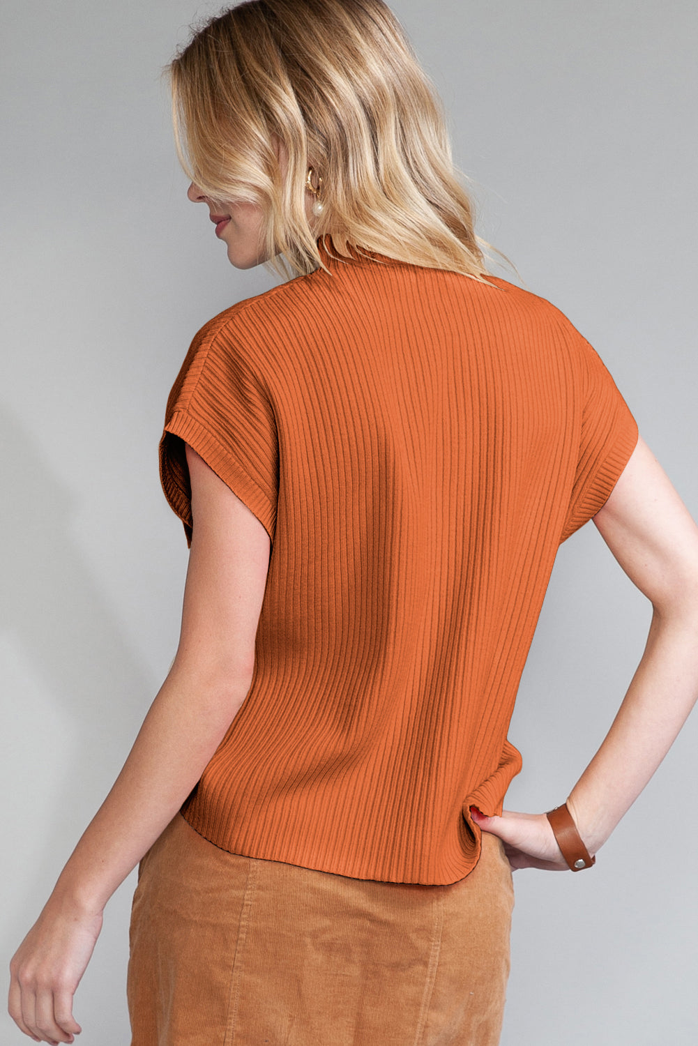 Woman wearing an orange ribbed top against a gray background
