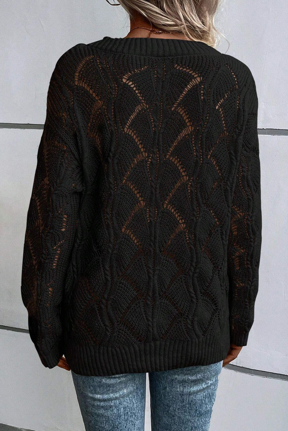 Black patterned sweater worn by a person against a white wall