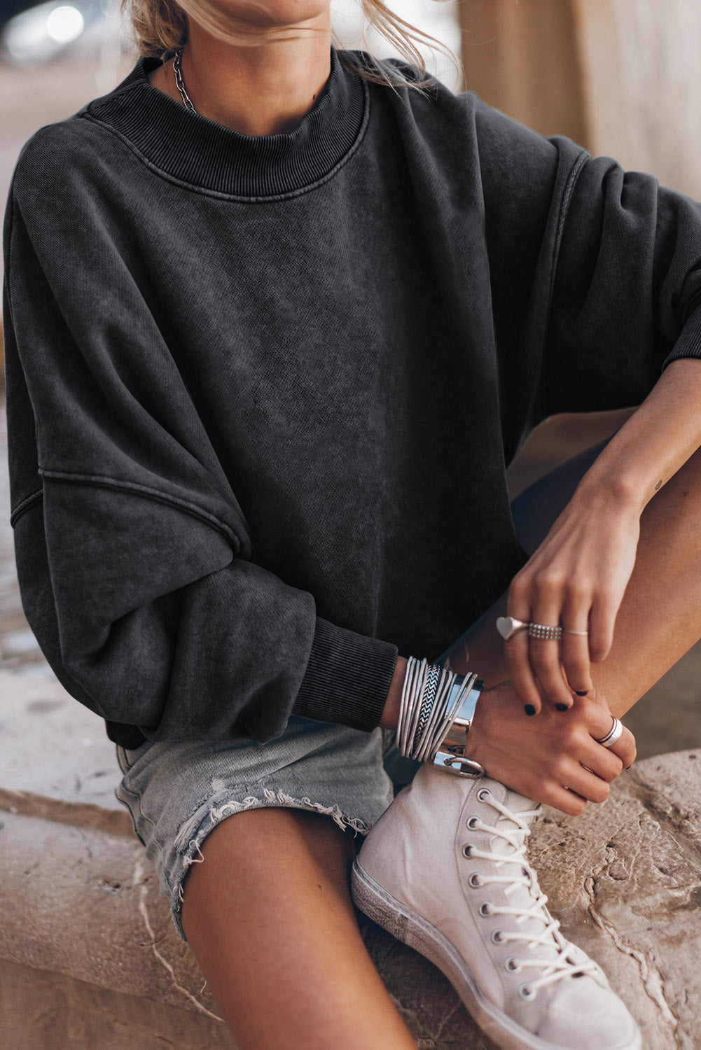 Person wearing a black oversized sweatshirt and white sneakers with bracelets on a blurred background