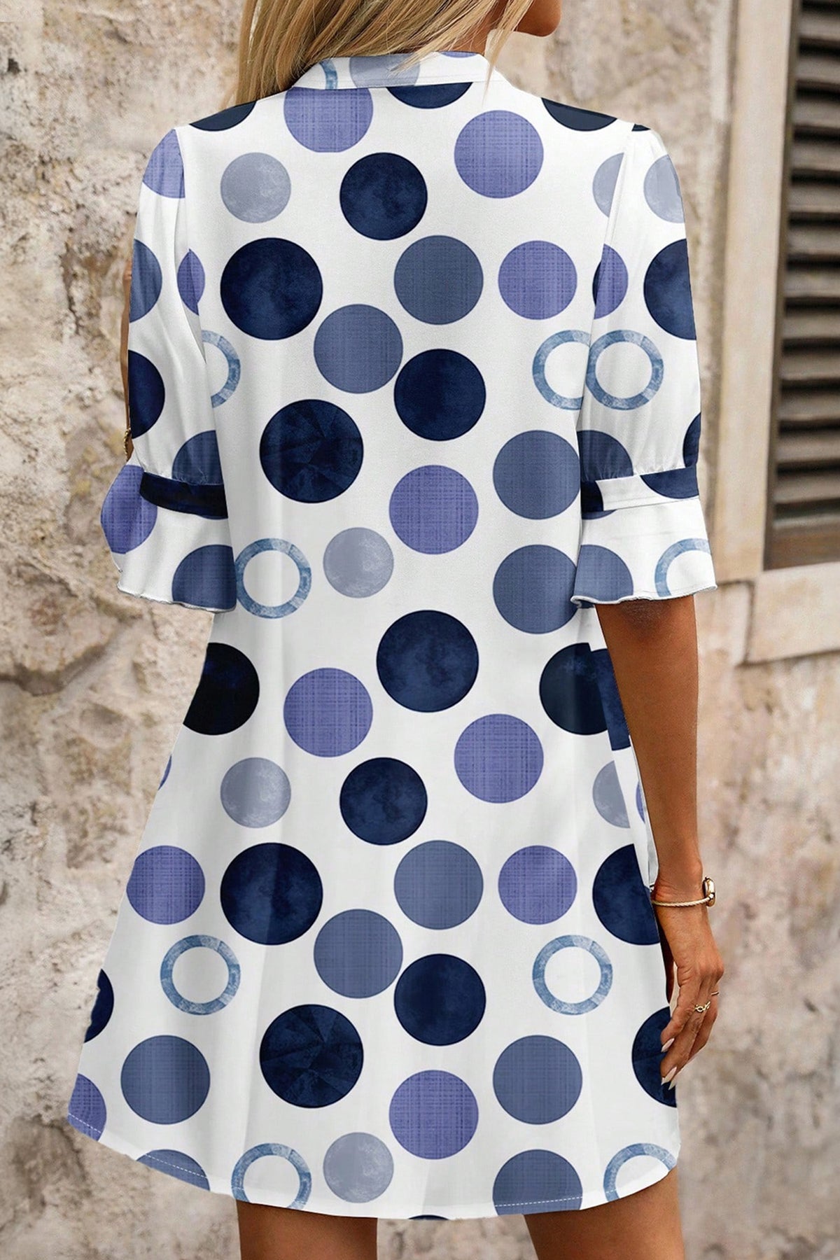 Woman wearing a polka dot blue dress with blue and white pattern against a stone wall.