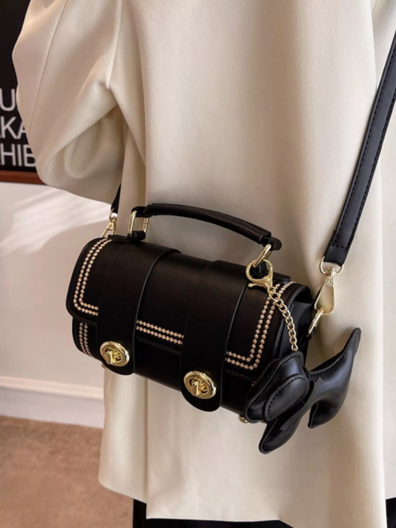 Black handbag with gold accents worn by a person in a white coat.