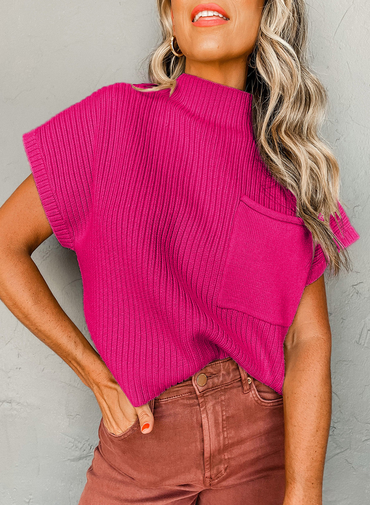 Woman wearing a bright pink sleeveless sweater against a gray background