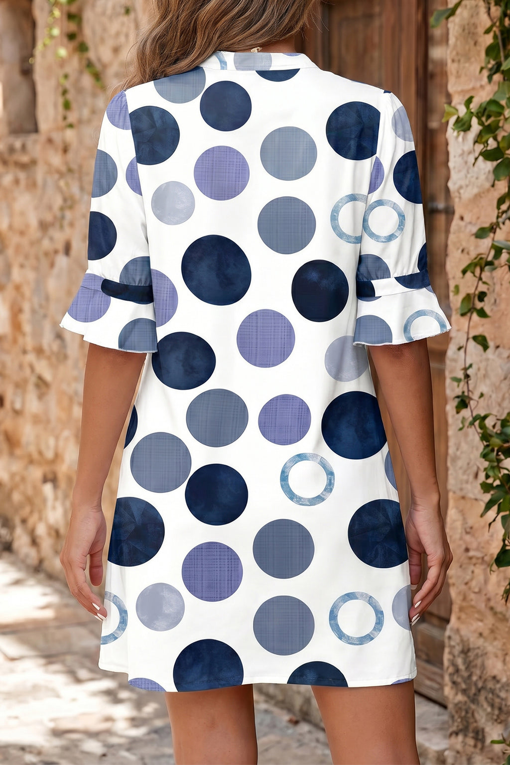 Woman wearing a polka dot blue dress with a neutral background back view