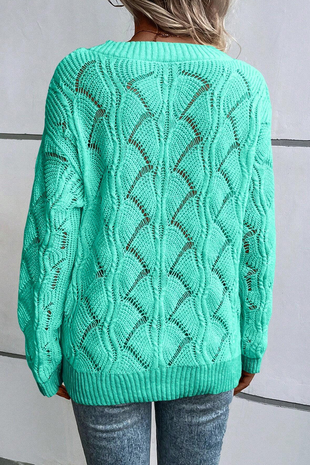 Green knitted sweater with a geometric pattern worn by a person against a neutral background