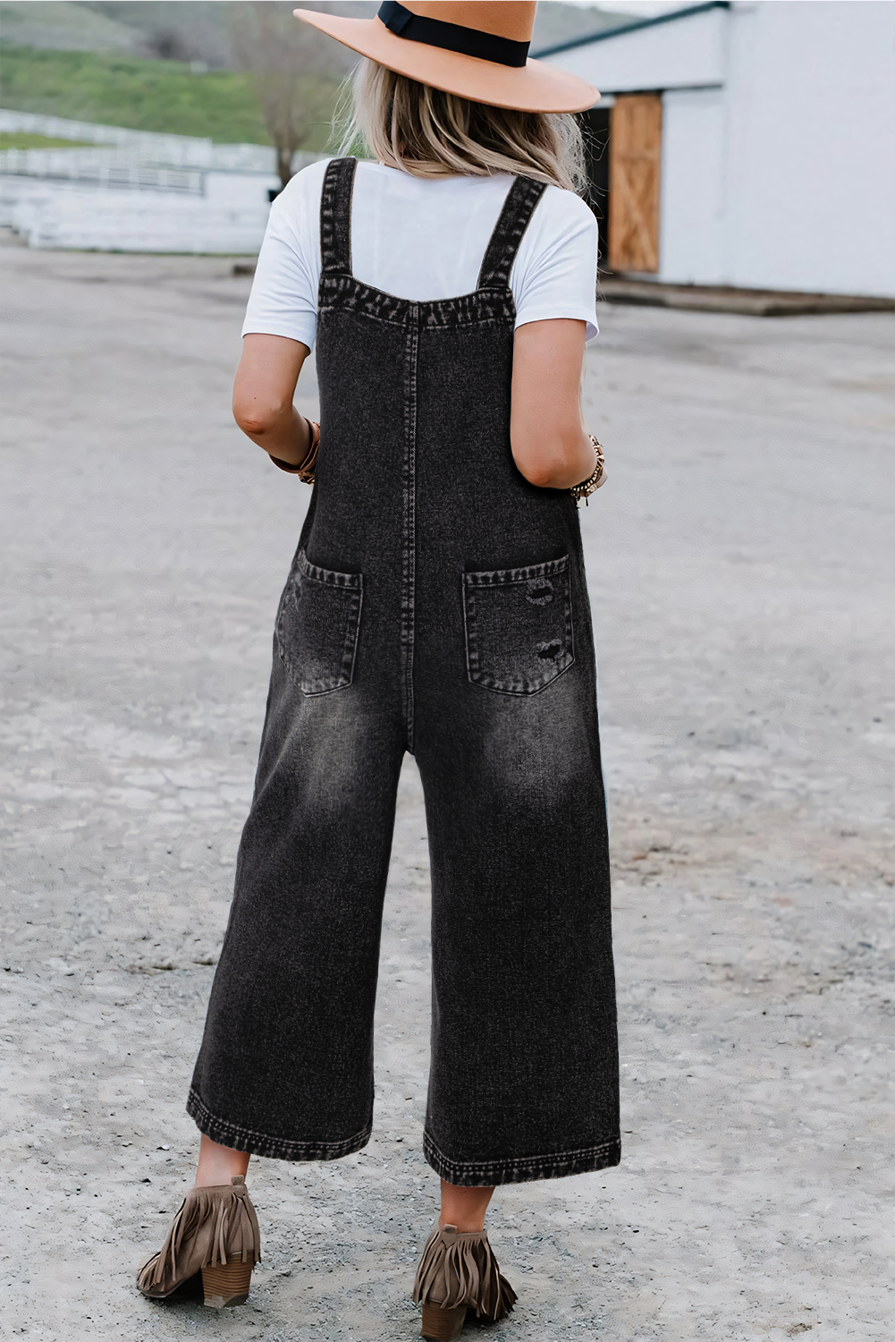 Person wearing black denim overalls and a white shirt outdoors.