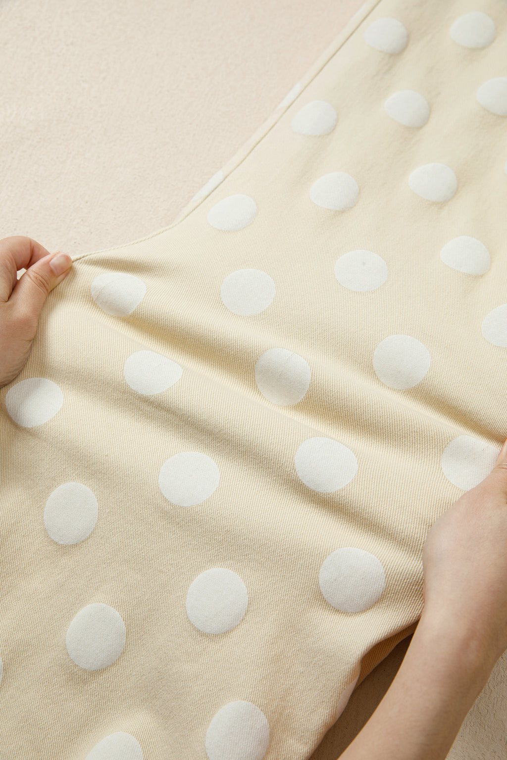 Beige fabric with white polka dots held by a hand