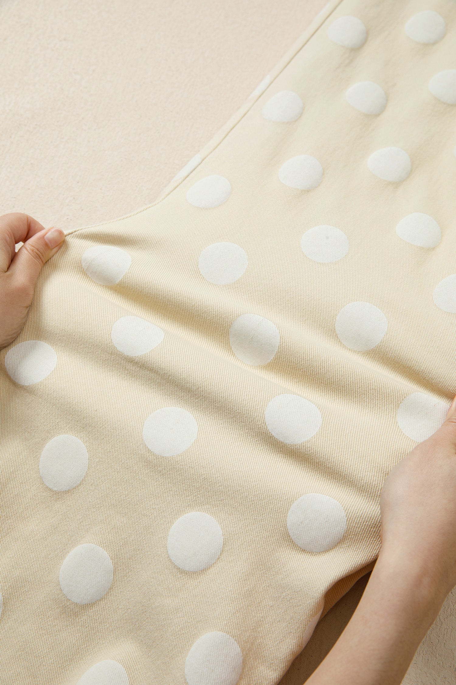 Beige fabric with white polka dots held by a hand