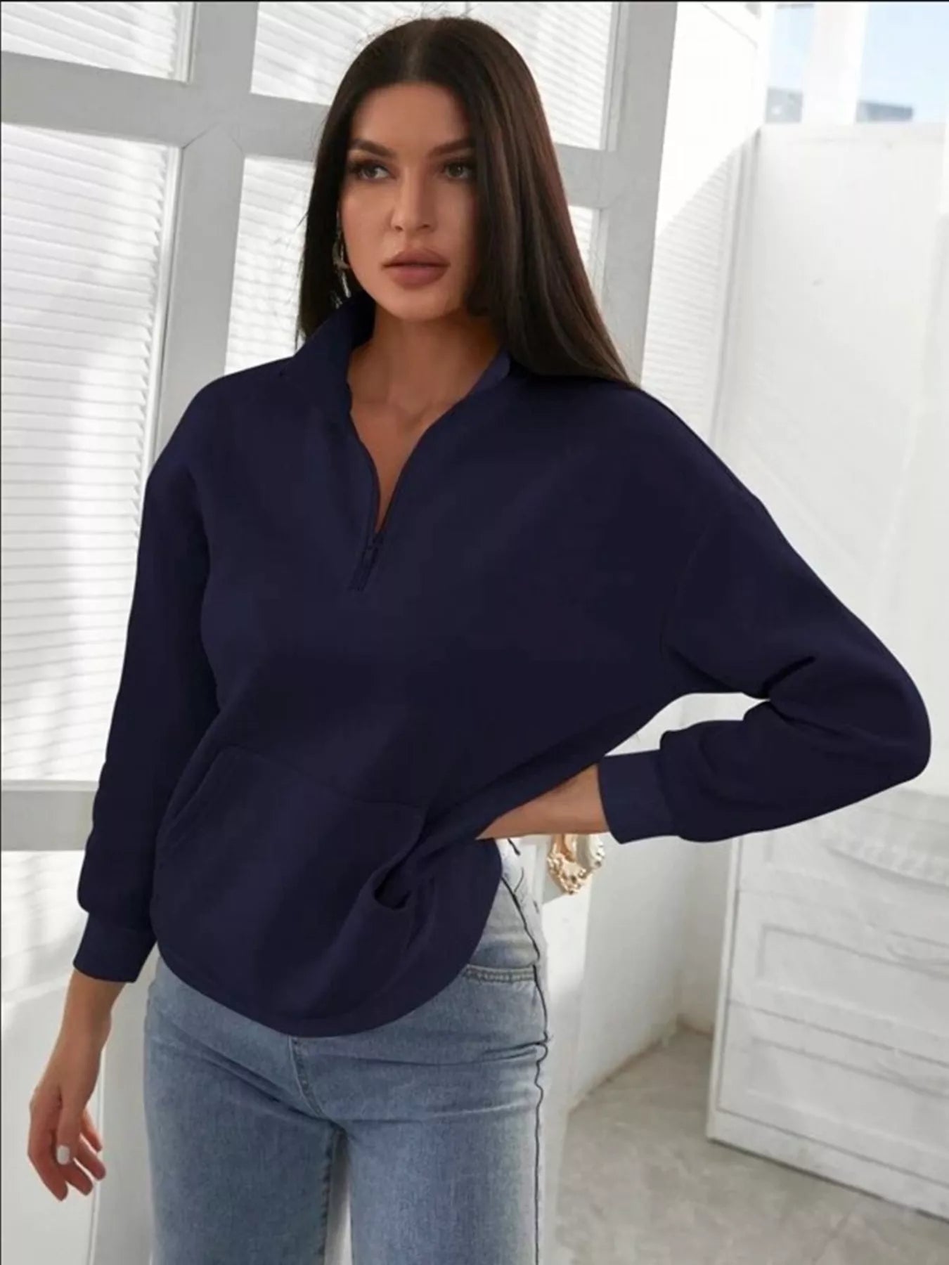 Woman wearing a navy blue sweater and light blue jeans indoors.