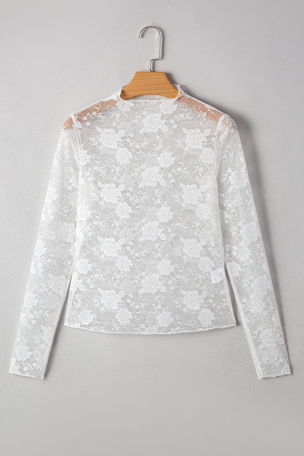 White lace long-sleeve top on a hanger against a gray background