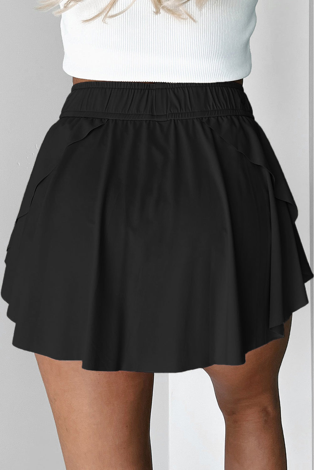 Black tennis skort worn by a person on a plain background back view