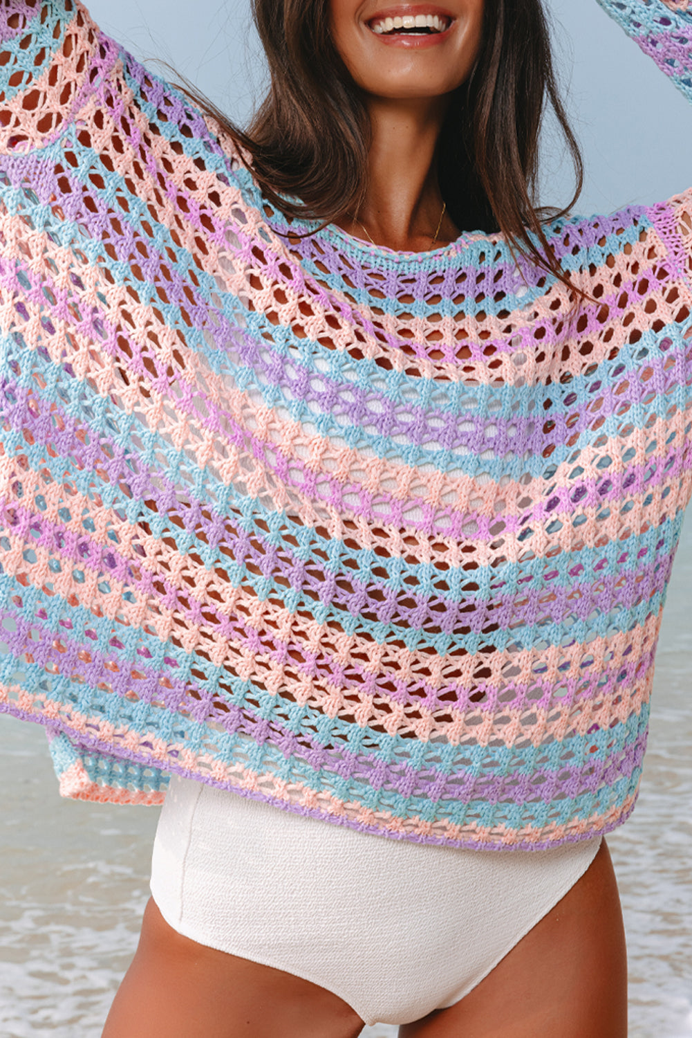 Woman wearing a colorful striped crochet poncho on a beach.