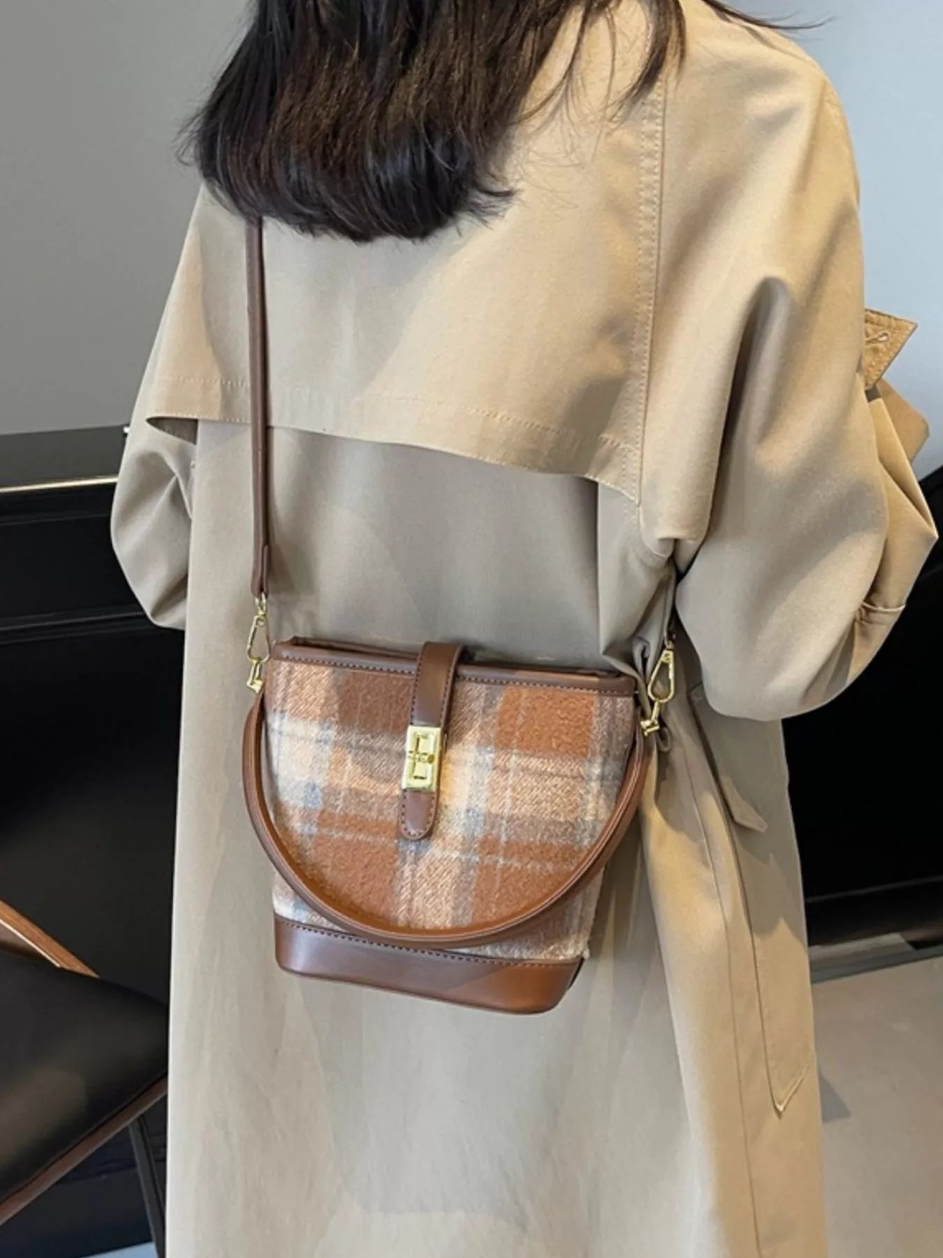 Person wearing a beige coat with a plaid crossbody bag.