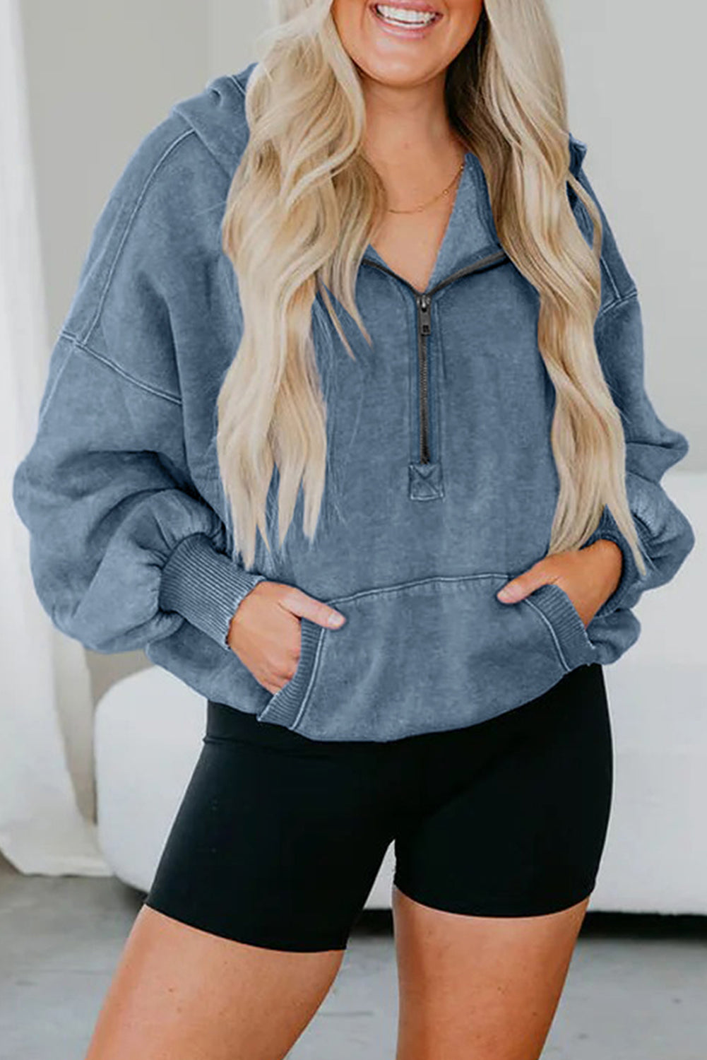 Person wearing a blue hoodie and black shorts with a neutral background