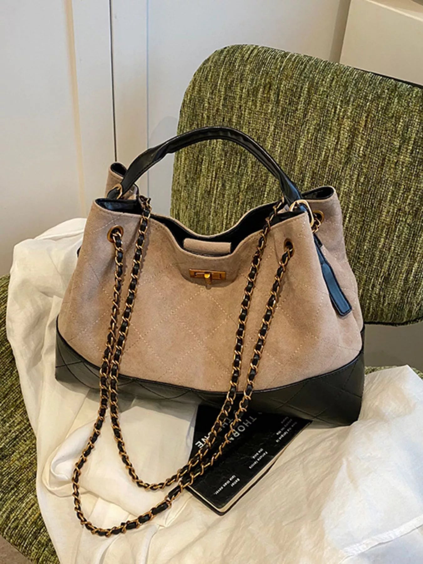 Beige handbag with black accents and a chain detail on a white surface.