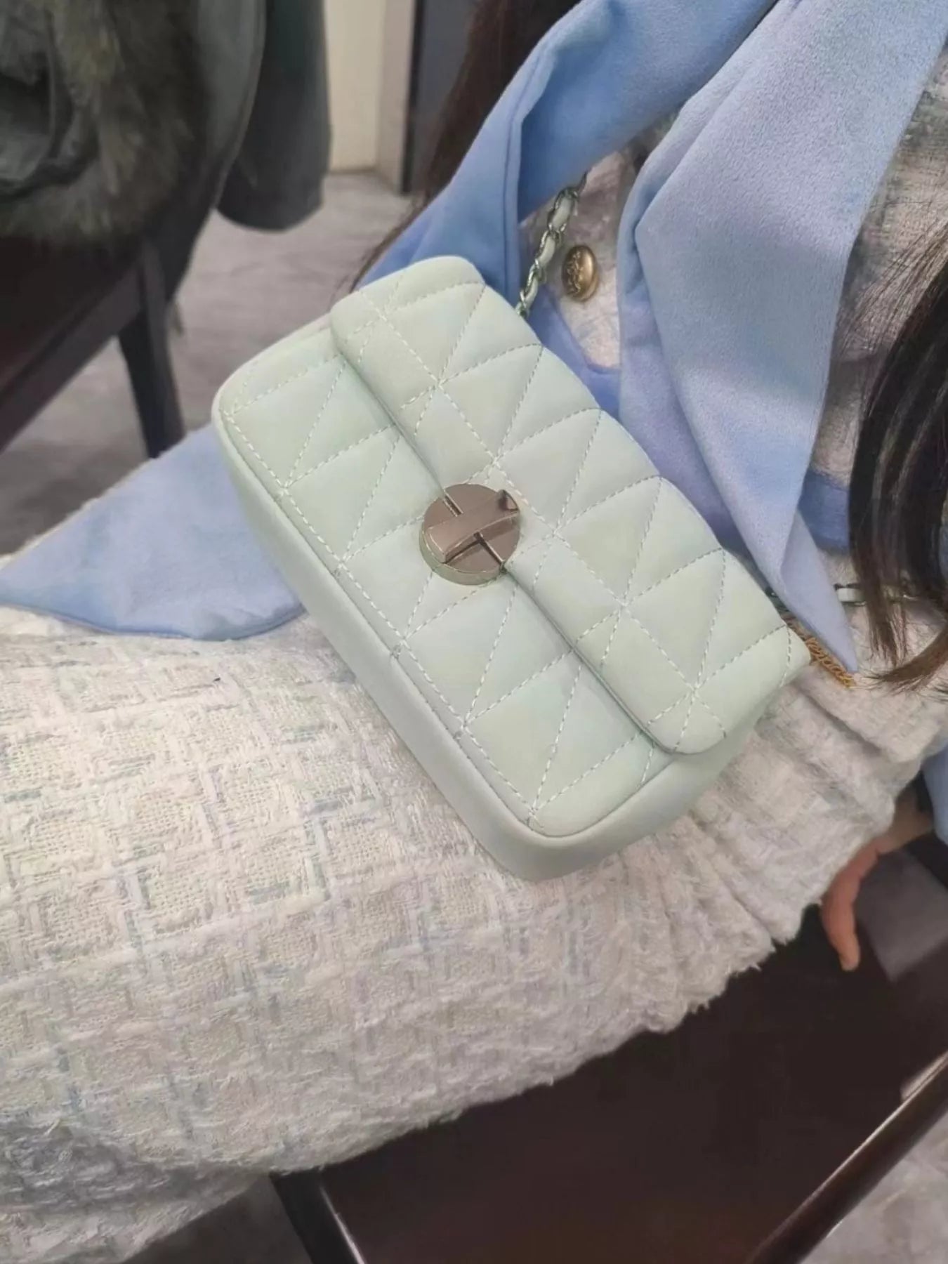 Light green quilted handbag with gold clasp held by a person wearing a light blue jacket.