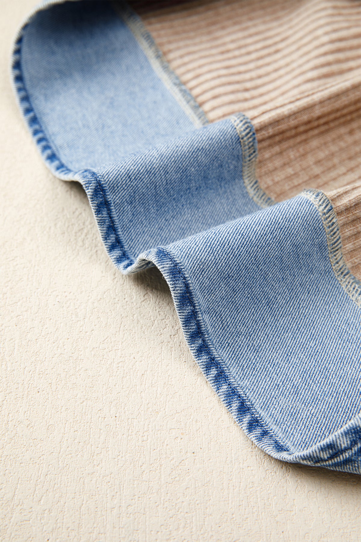 Close-up of a beige  blouse with blue denim fabric edge on a beige surface