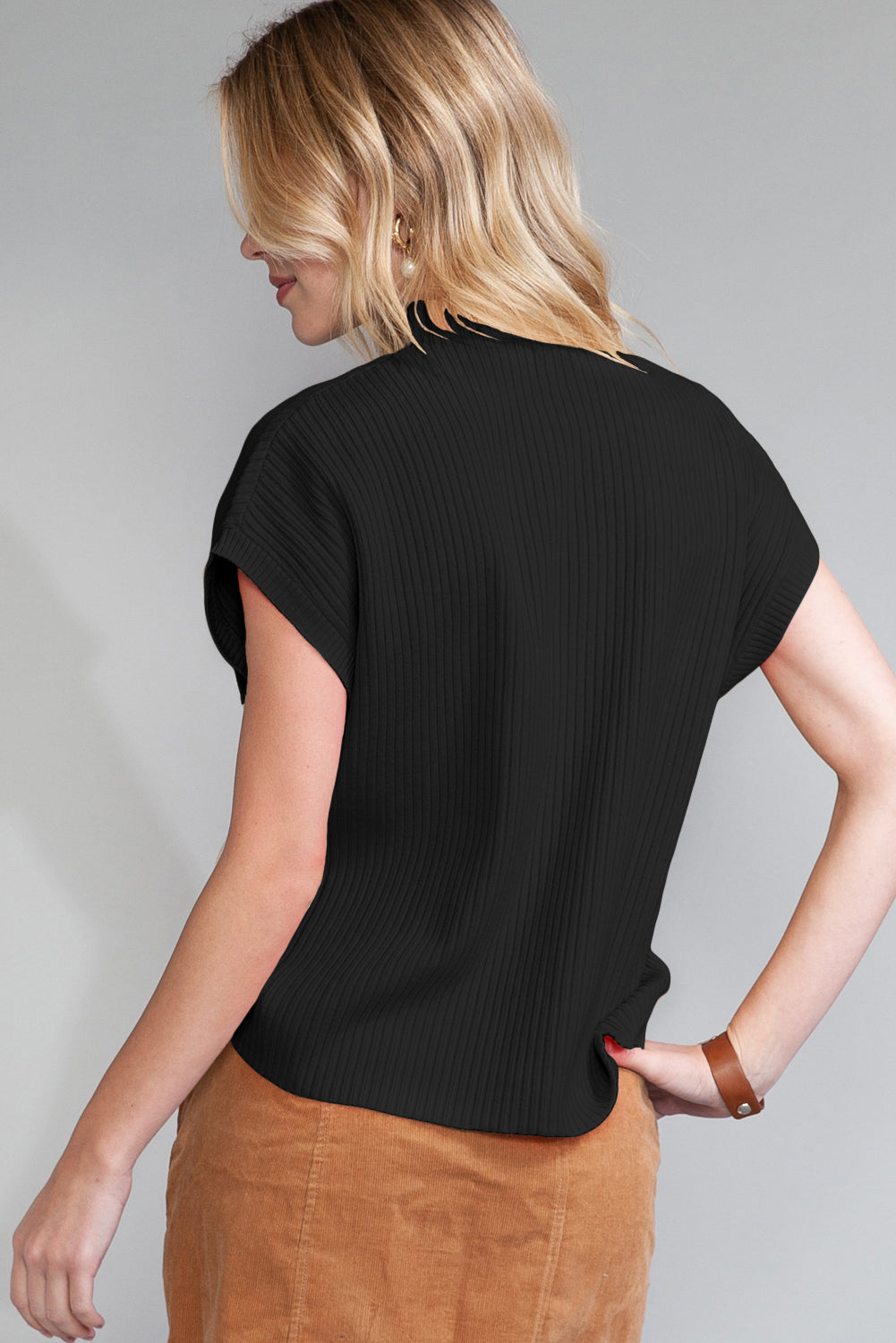 Woman wearing a black t-shirt and brown pants against a gray background