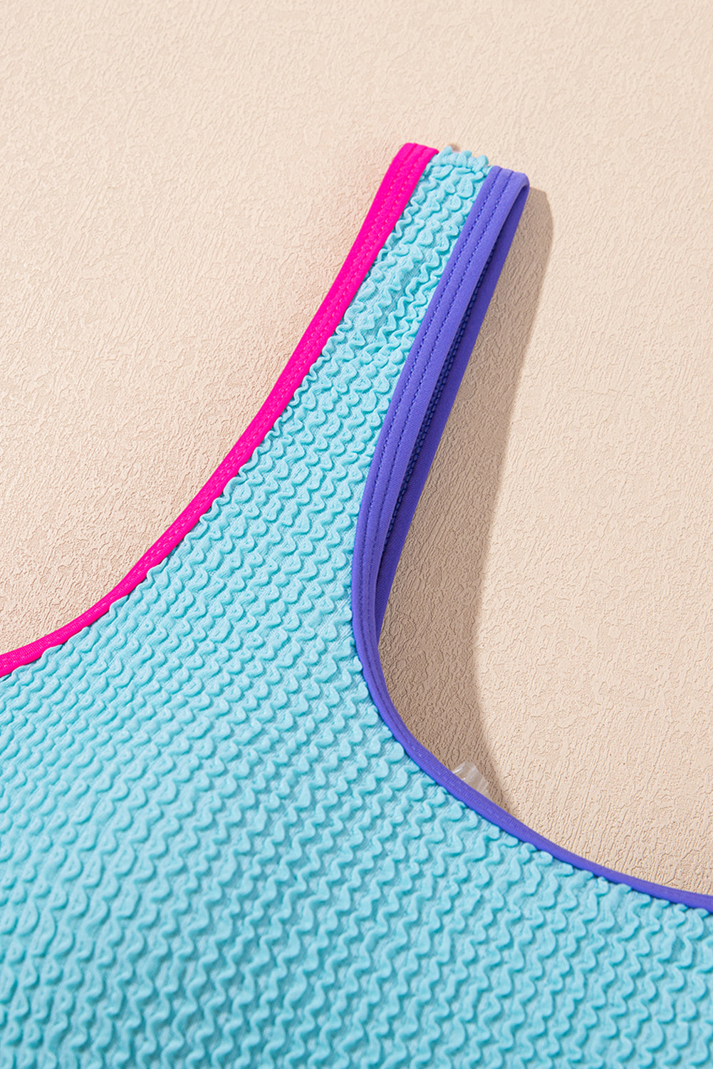 Close-up of a blue textured bikini top with pink and purple trim on a beige background