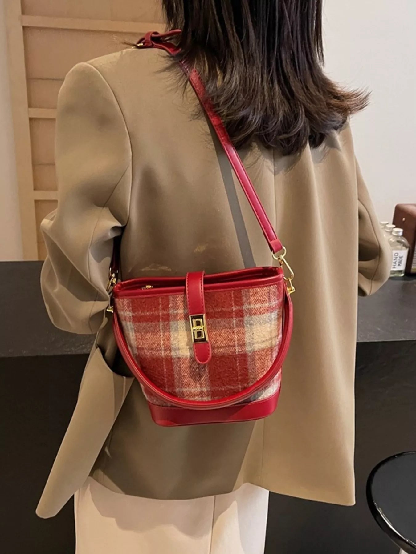 Person wearing a beige coat with a red plaid handbag over one shoulder.