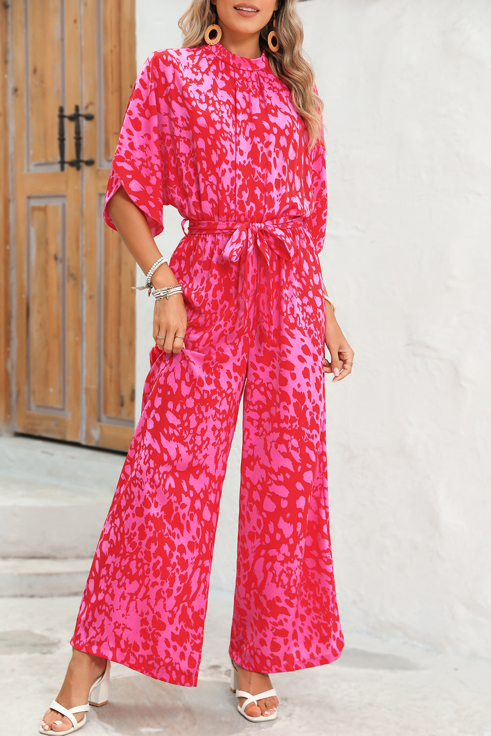 Woman wearing a pink patterned jumpsuit standing against a white wall.