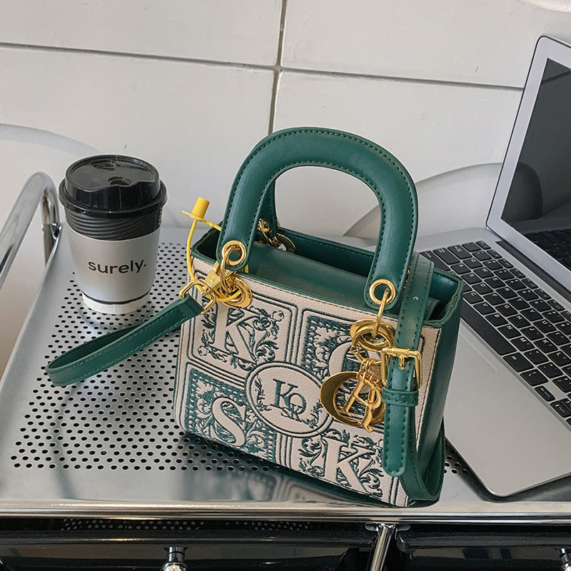 Green handbag with gold chain on a desk next to a laptop and coffee cup.