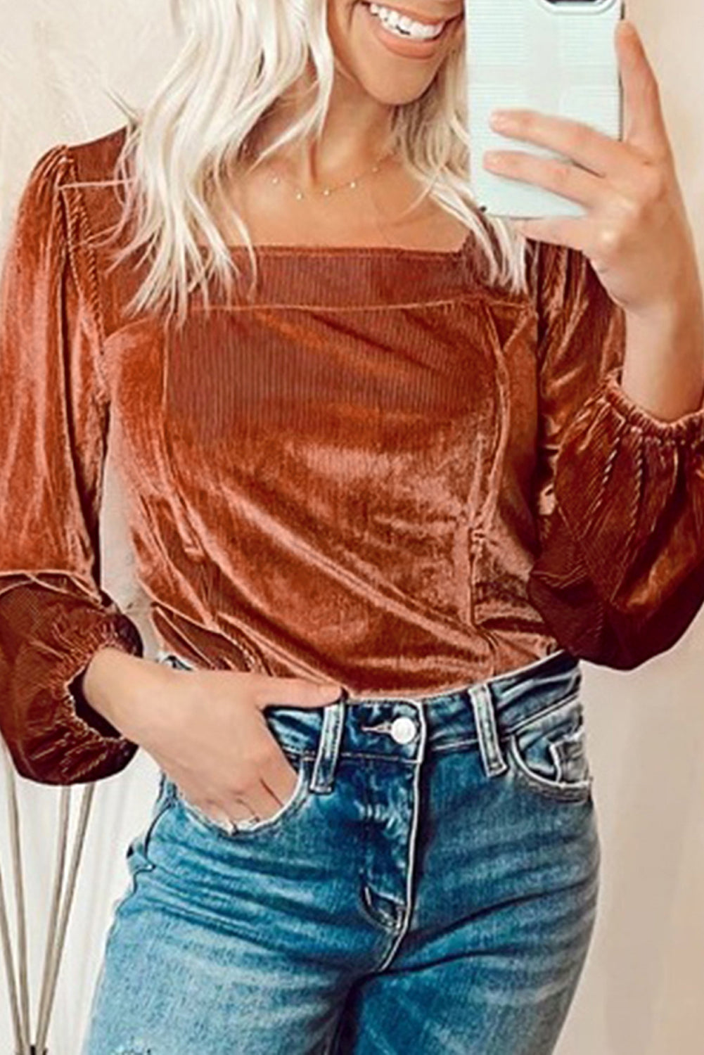 Person wearing a brown velvet top and blue jeans, taking a mirror selfie.