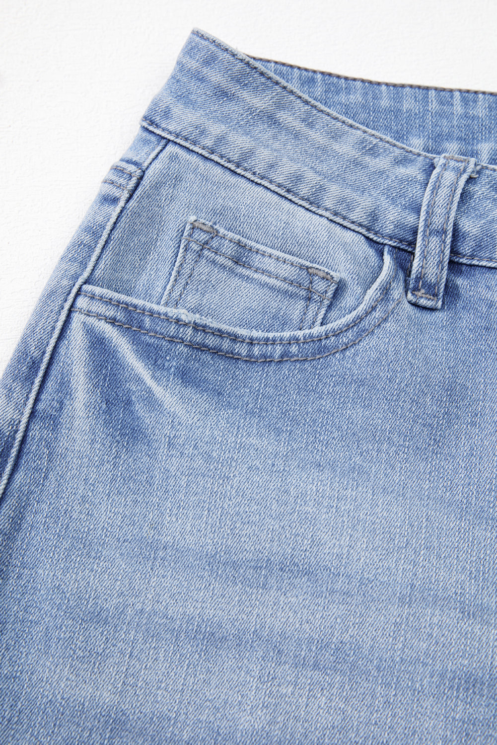 Close-up of blue denim jeans with a pocket detail on a light gray background