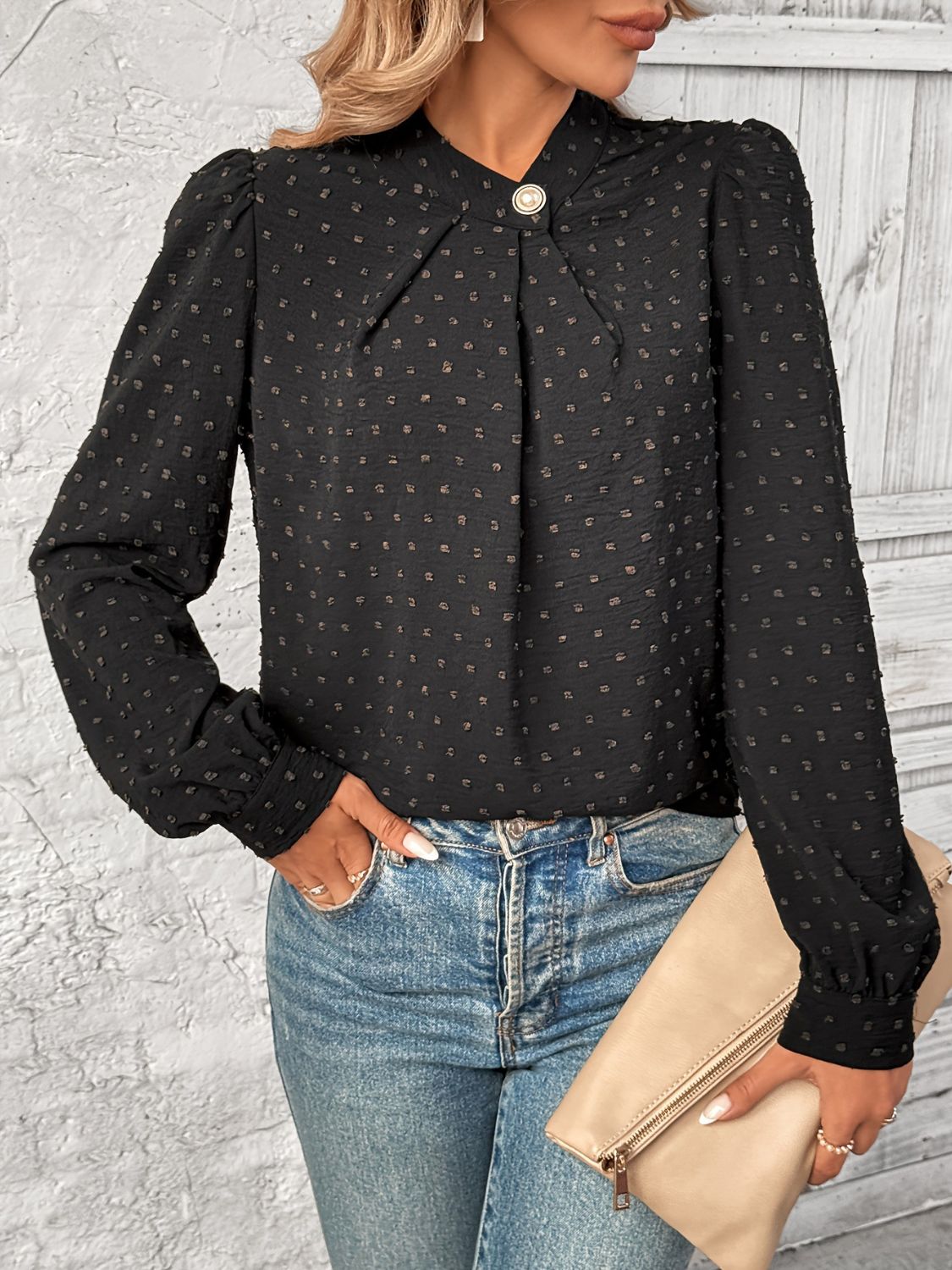 A woman wearing a black long sleeve blouse with a Swiss dot pattern holding a purse