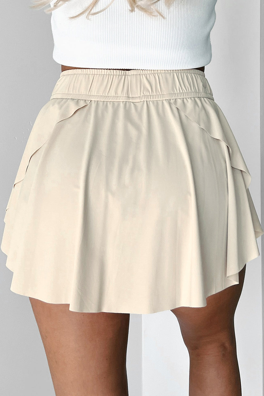 Beige tennis skort worn over a white top on a plain background back view