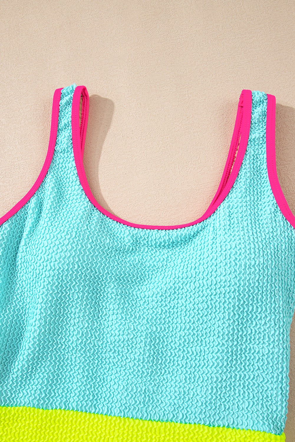 Blue tank top with pink trim and green bottom on a beige background