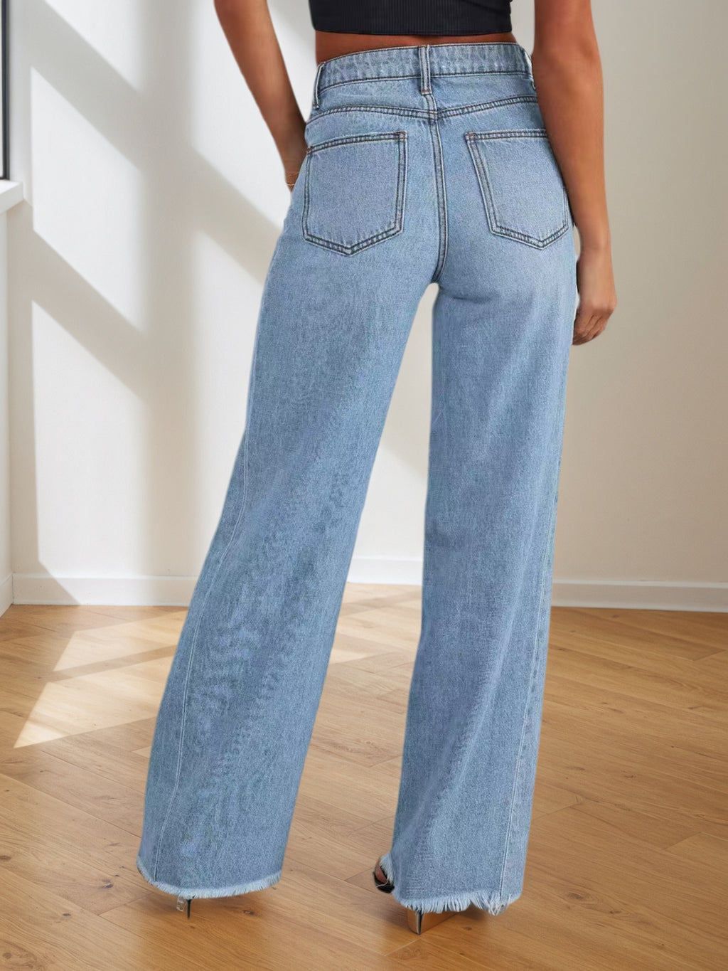 Person wearing light blue wide-leg jeans in a room with wooden floor and white walls.