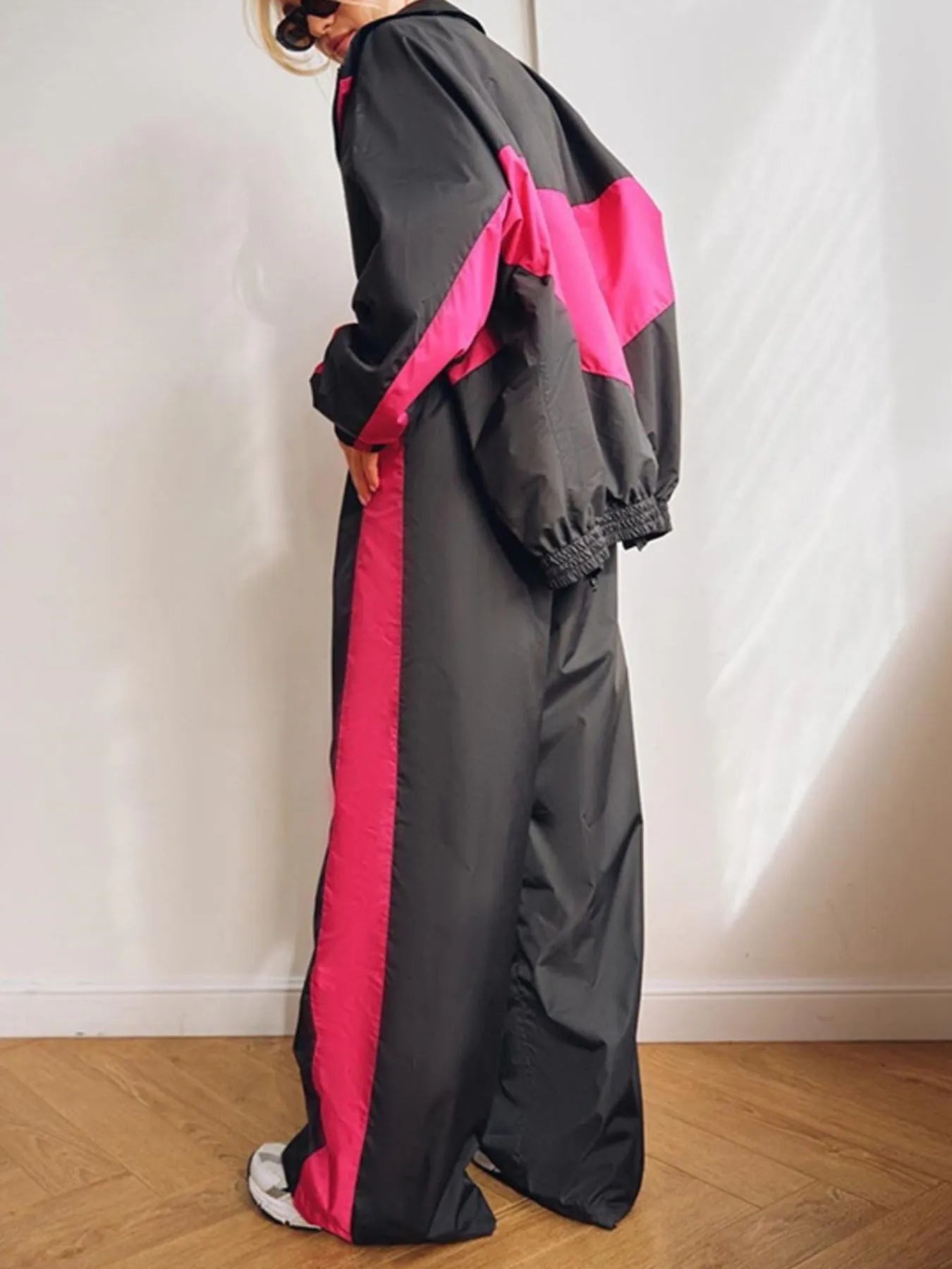 Person wearing a gray and pink tracksuit against a white wall.