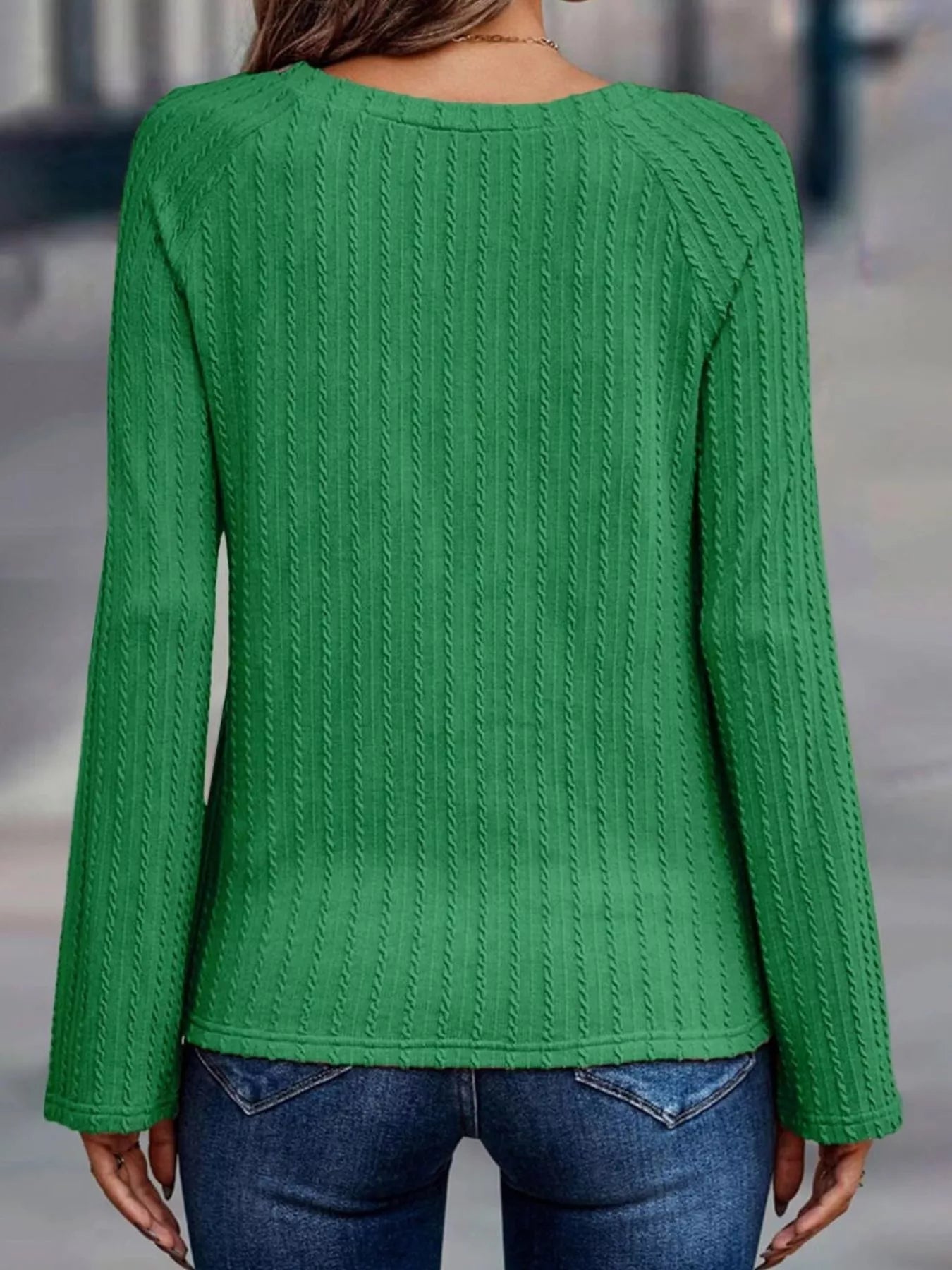 Green cable knit sweater worn by a person on a blurred background