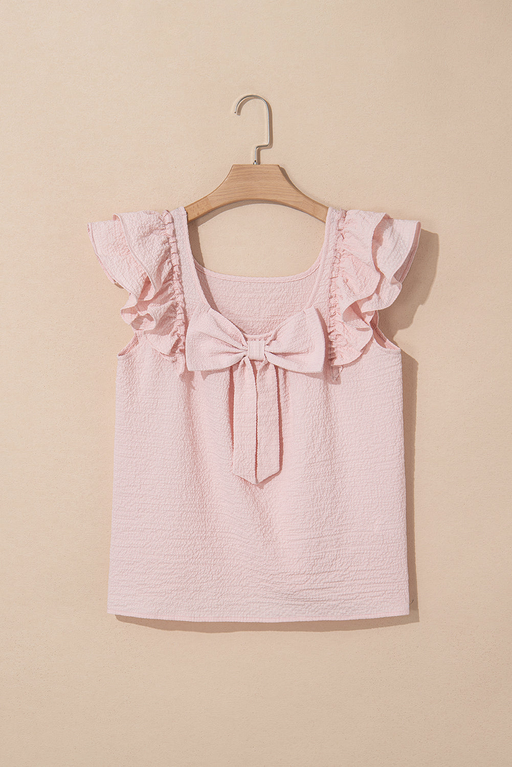 Pink top with ruffled straps and a bow on a beige background