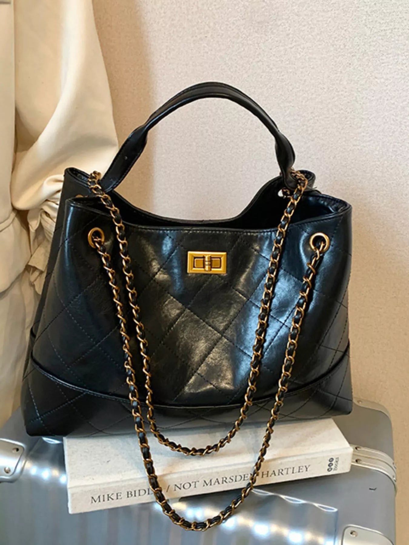 Black quilted handbag with gold chain on a suitcase