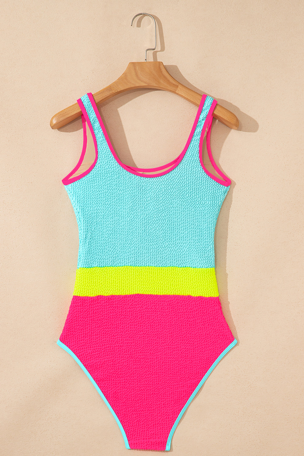 Color-blocked swimsuit with pink, blue, and green on a beige background