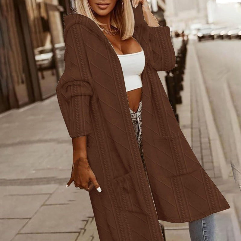 Woman wearing a brown knitted cardigan over a white top and jeans on a city street.