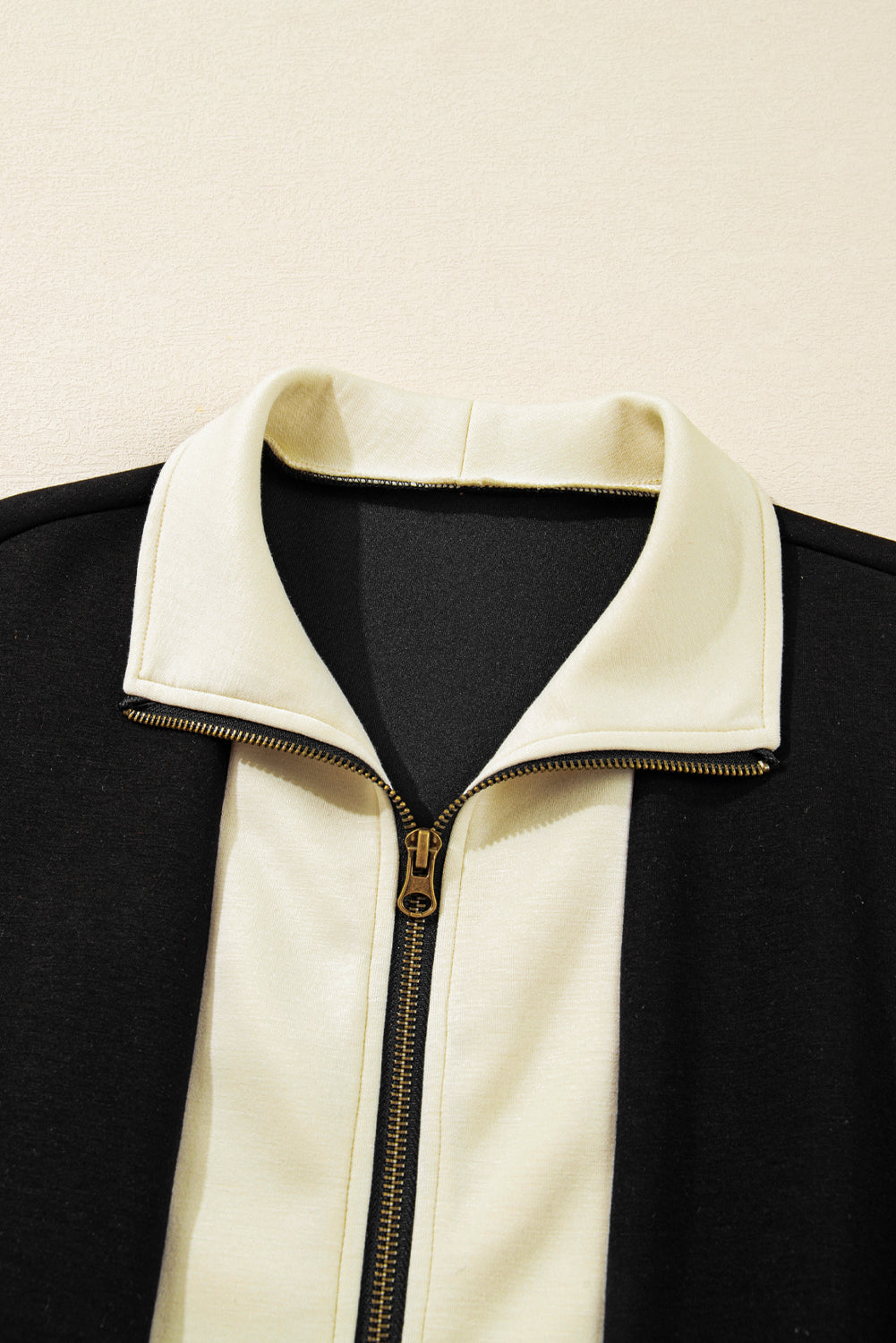 Black jacket with a white collar and gold zipper on a beige background