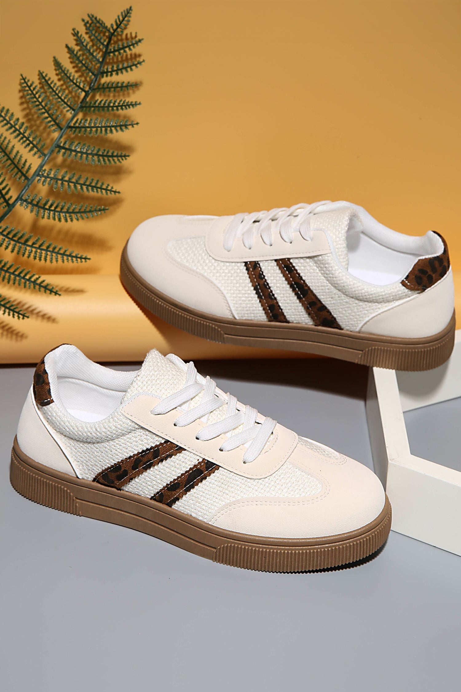 White sneakers with brown soles and stripes on a gray surface with a yellow background