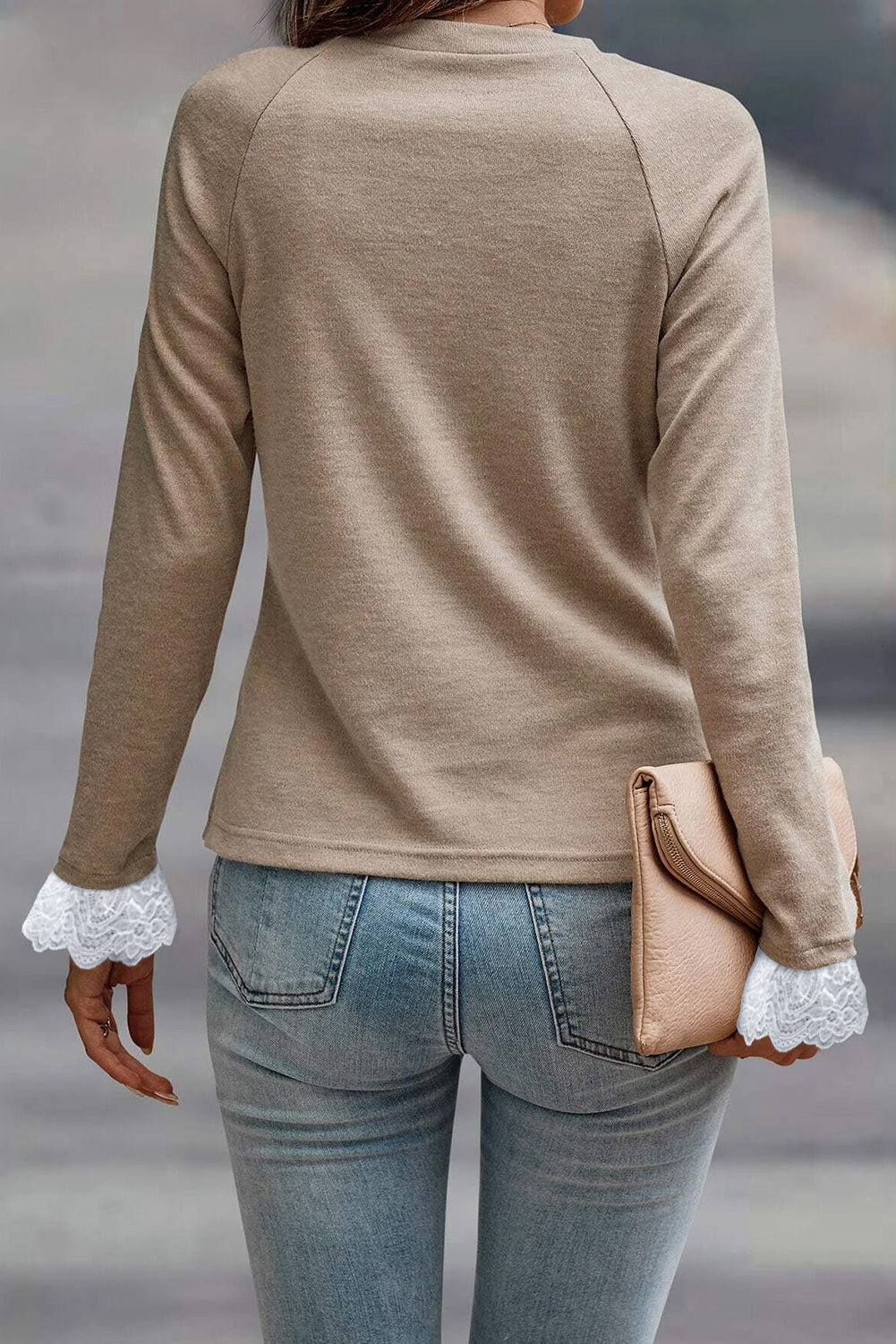 Person wearing a beige long-sleeve top with lace cuffs and holding a beige clutch.