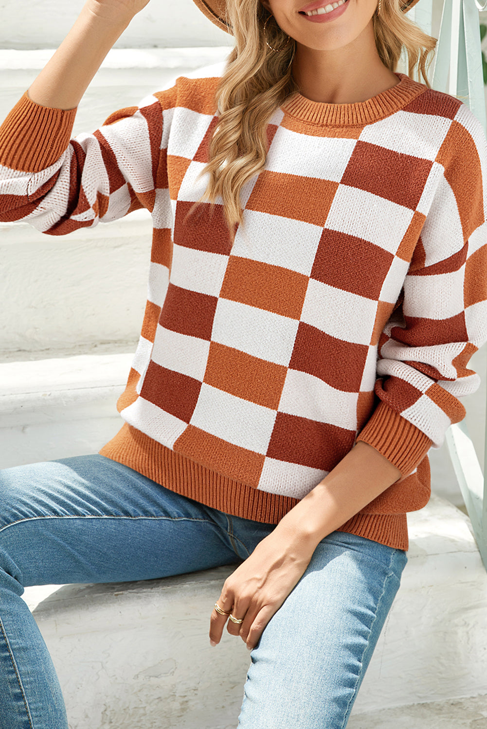 Woman wearing a checkered sweater with orange and white pattern sitting on steps.