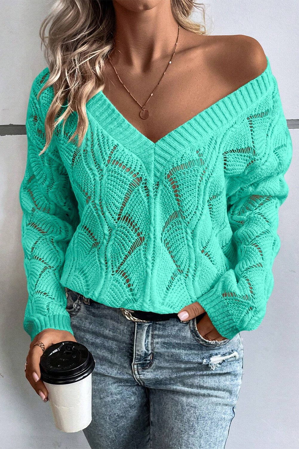 Person wearing a teal sweater with a textured pattern, holding a coffee cup.
