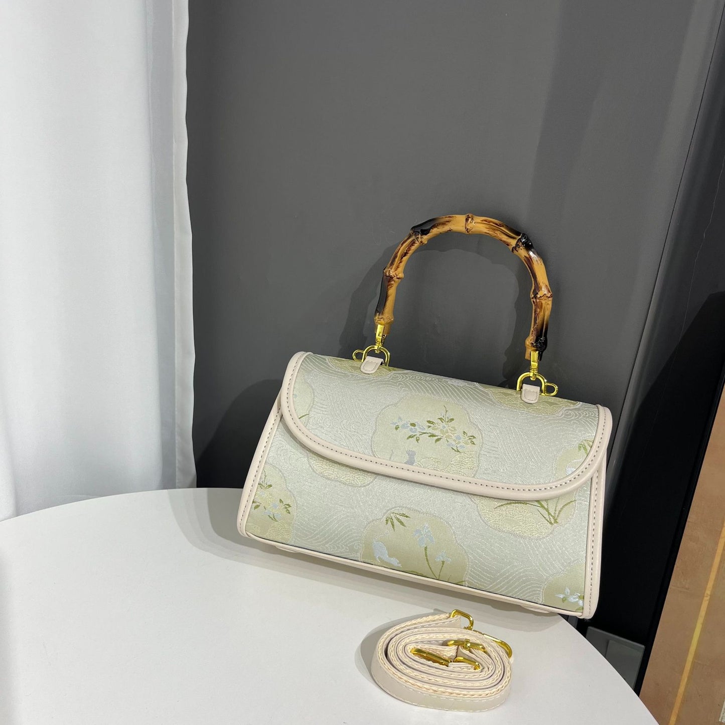 Light green handbag with floral pattern and gold accents on a white surface.