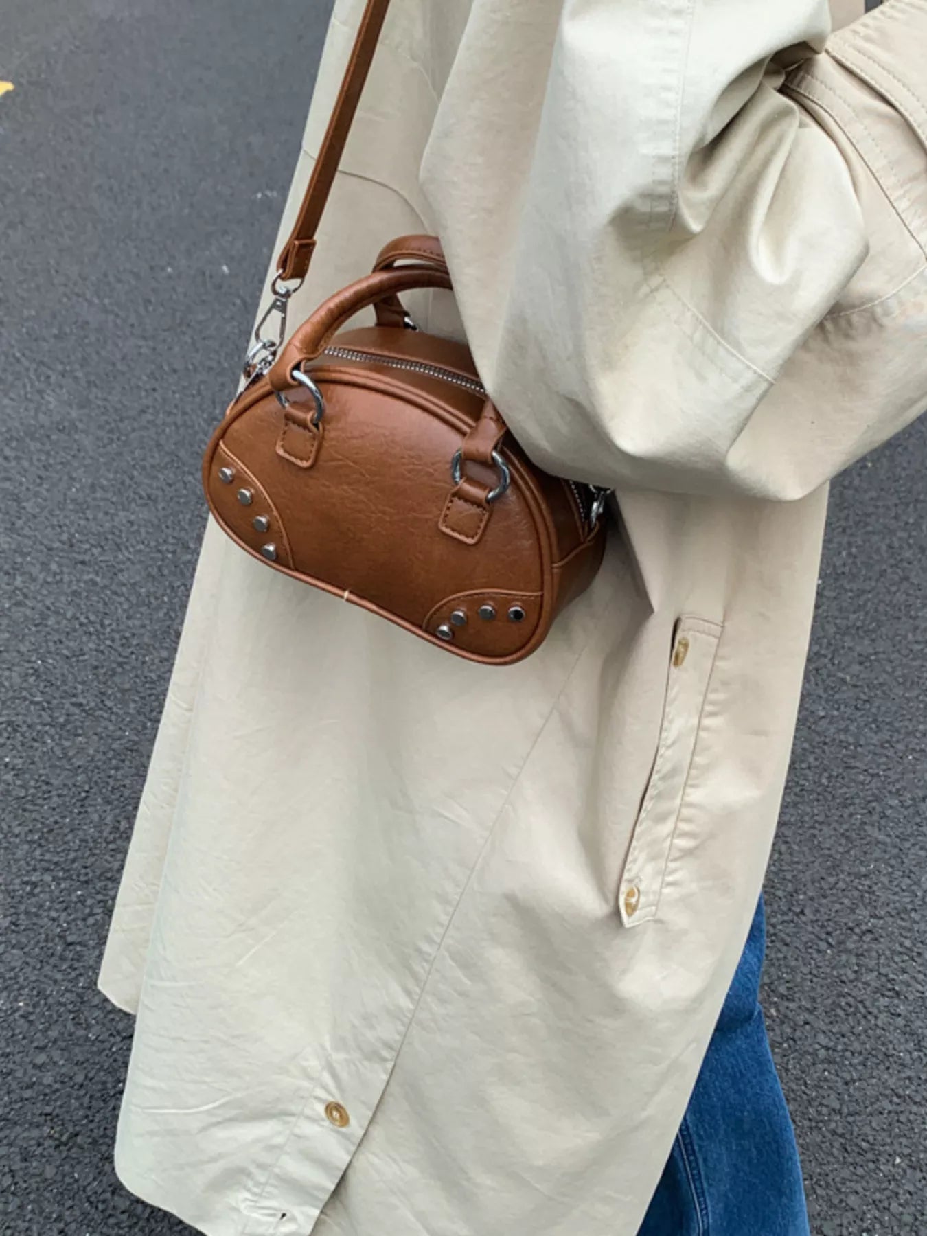 Person wearing a beige coat holding a brown handbag on a dark surface