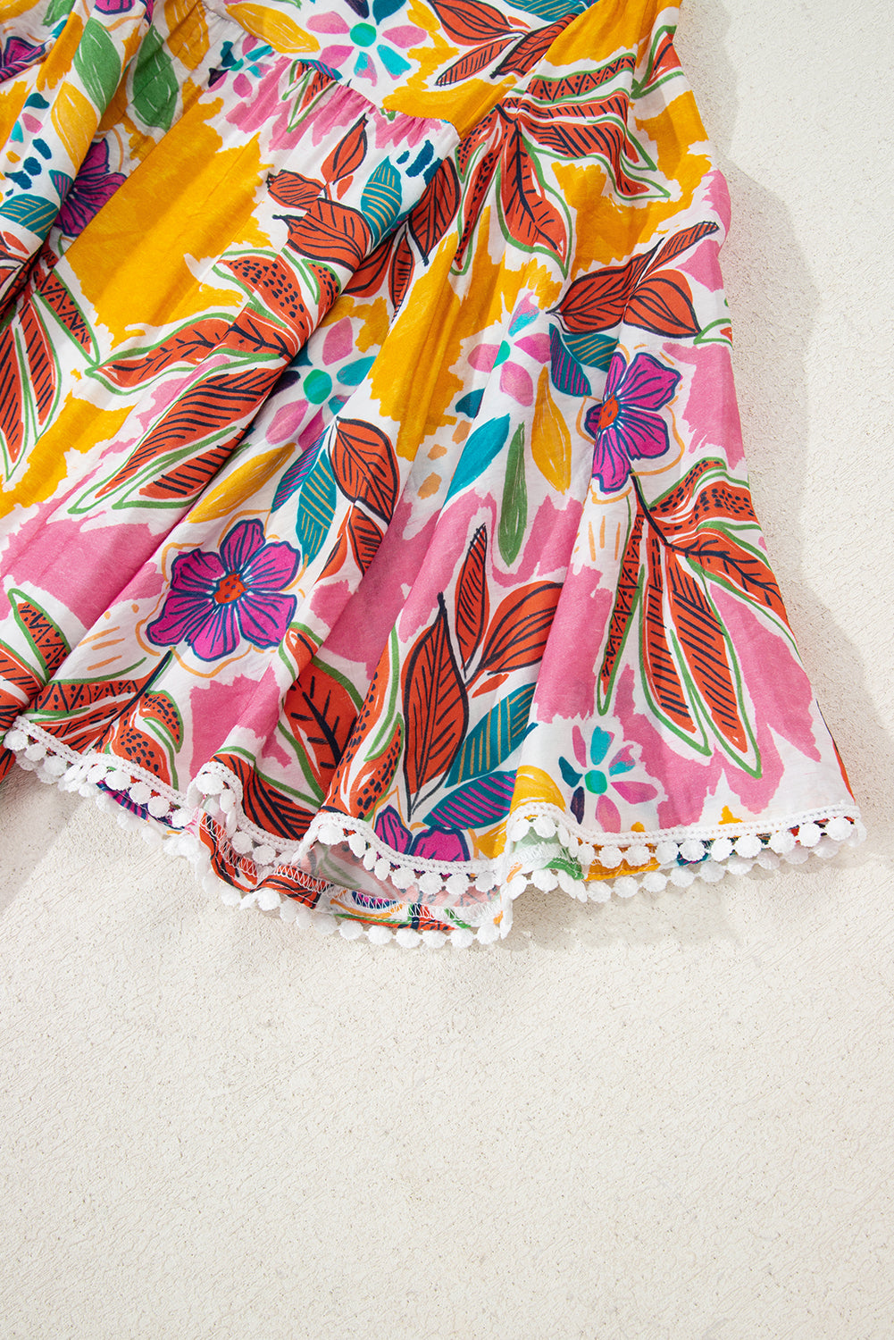 Close-up of the flared hem of a colorful floral dress featuring pink and yellow shades with delicate lace trim.